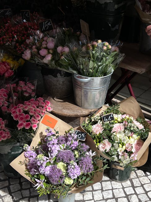 A display of fresh floral arrangements and bouquets at a flower shop, featuring a variety of pink, purple, and white flowers. In the foreground, there are two bouquets wrapped in brown paper: one with